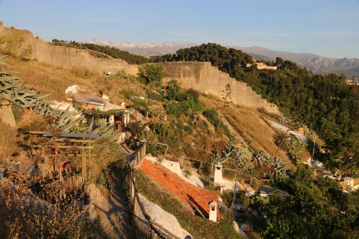 Huleboliger og haver på Sacromonte-skråningen, med en stenmur ovenover og Sierra Nevada i det fjerne